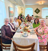 Large group gathered at a decorated dining table with flowers.