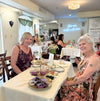 Women enjoying tea and pastries at a long dining table.