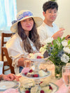 Two person smiling at a tea table with pastries and flowers.