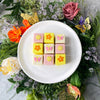 Yellow floral petit fours on a white plate with a colorful flower backdrop.