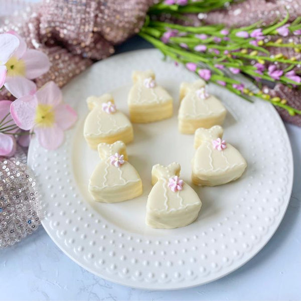 White dress petit fours decorated with pastel flowers on white plate.