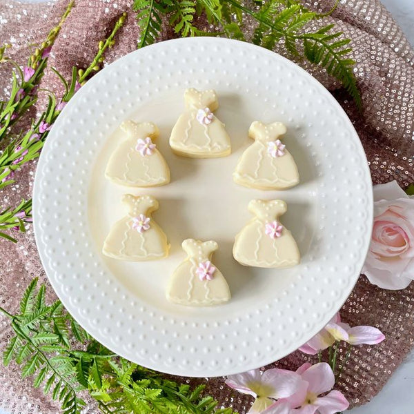 White dress petit fours decorated with pastel flowers on white plate.