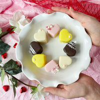 Heart-shaped petit fours in pink, yellow, and chocolate on white plate.