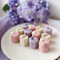 Assorted pastel petit fours with purple floral backdrop.