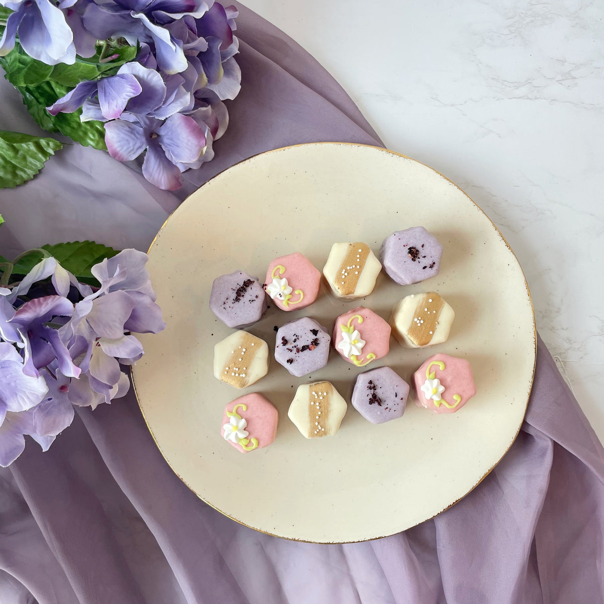 Assorted pastel petit fours with purple floral backdrop.