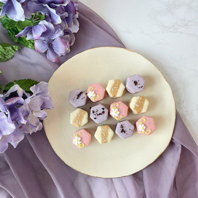 Assorted pastel petit fours with purple floral backdrop.