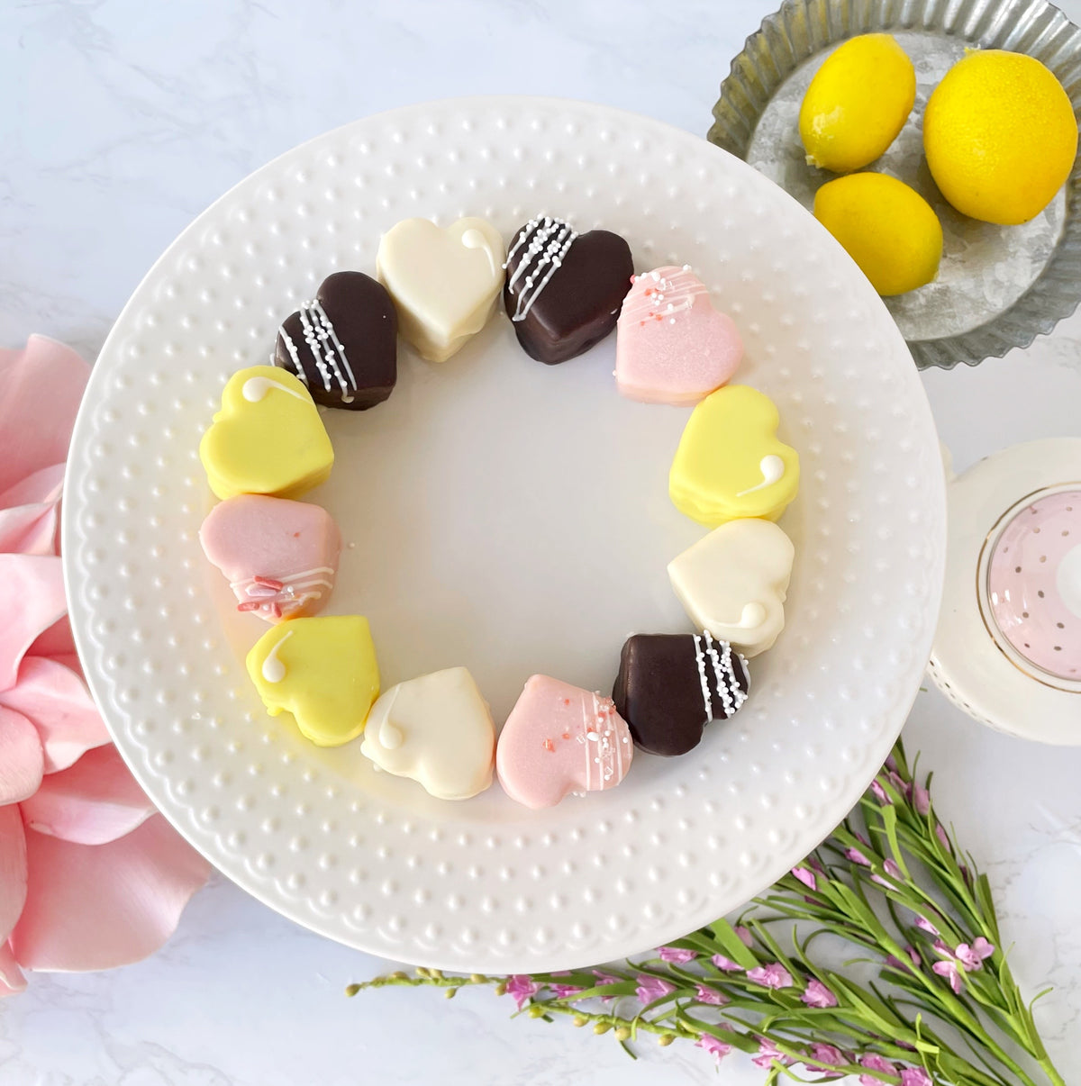 Circle arrangement of heart-shaped petit fours on white plate with lemons.