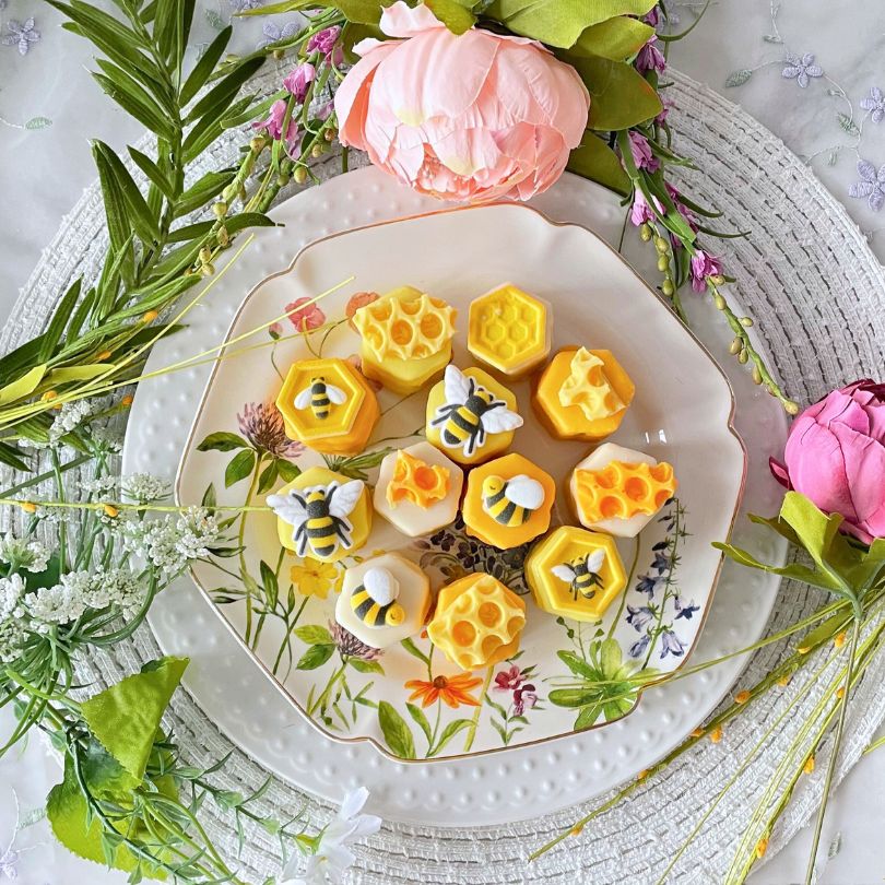 Plate of yellow petit fours surrounded by pink flowers and greenery.