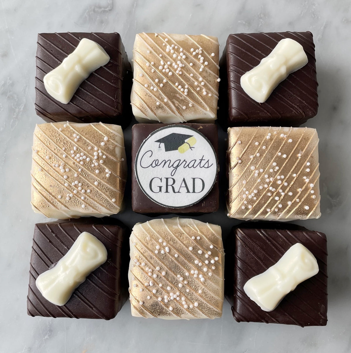 chocolate-coated and champagne-colored white chocolate coated petit fours with 'Congrats Grad' label on a marble surface