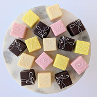 Assorted pastel petit fours arranged on white plate.