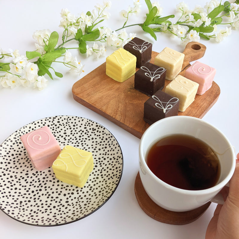 Tea set with plate of pastel petit fours on wooden board.