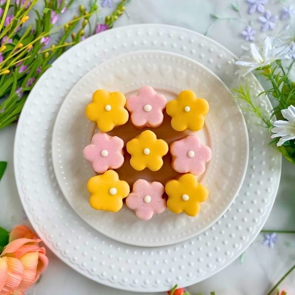 tiny genoise cakes decorated as pink and yellow flowers on a white plate with floral background