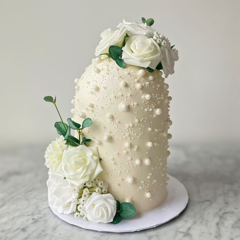 Decorative cake with white flowers and pearl-like embellishments on a marble surface.