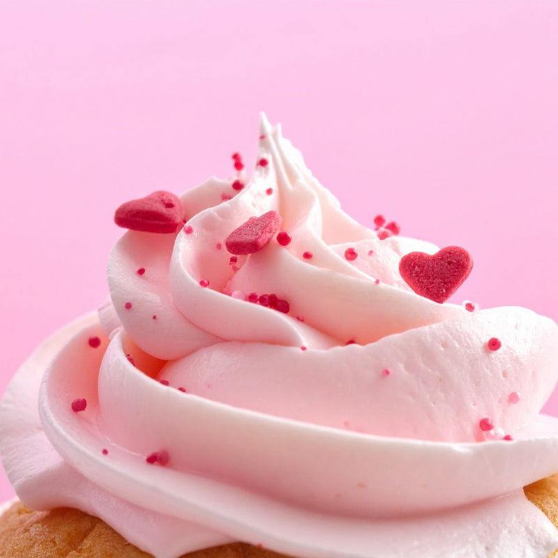 Close-up of a cupcake with pink frosting and heart-shaped sprinkles on a pink background