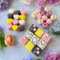 Mother's Day petit fours bundle featuring Mom tea cakes, heart-shaped petit fours, and elegant decorated tea cakes styled with spring flowers.