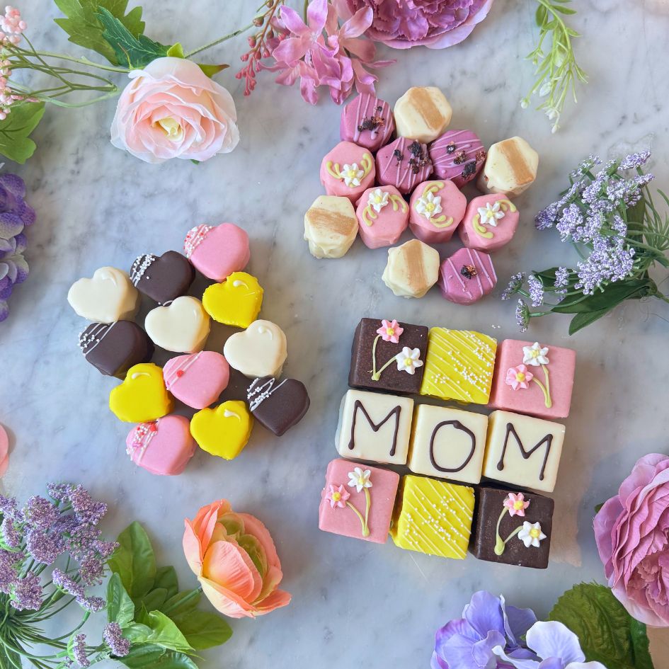 Mother's Day petit fours bundle featuring Mom tea cakes, heart-shaped petit fours, and elegant decorated tea cakes styled with spring flowers.