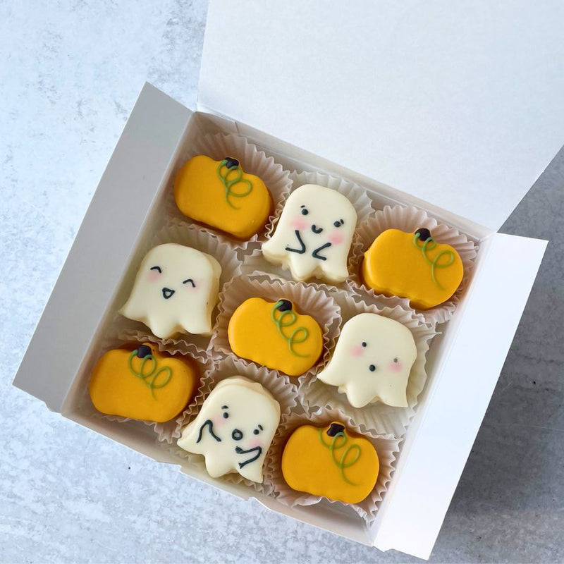 Box of Halloween-themed petit fours with ghost and pumpkin designs on a light background